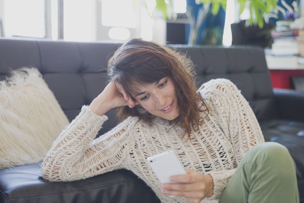 Female in wooly sweater taking video call on phone in comfy living room