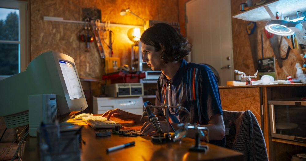 Portrait Of White Male Software Engineer Programming on Old Desktop Computer In Retro Garage In The Evening.