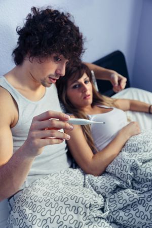Man showing thermometer to woman in bed