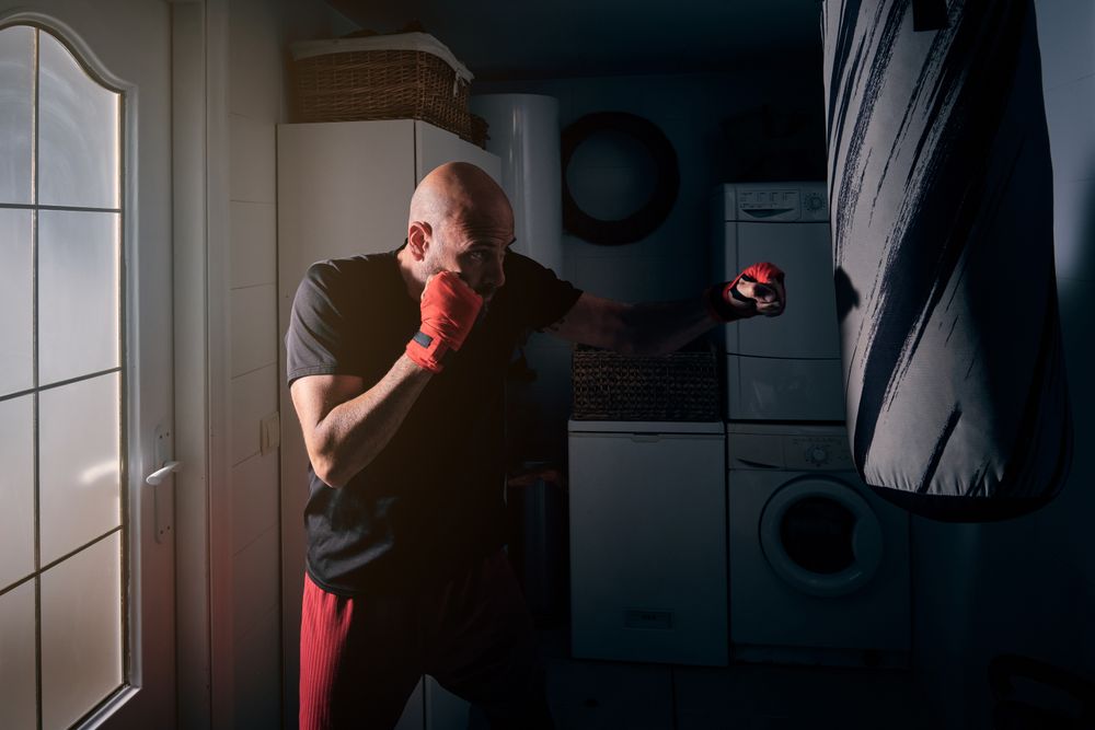 Man training boxing in the laundry room at home with a bag