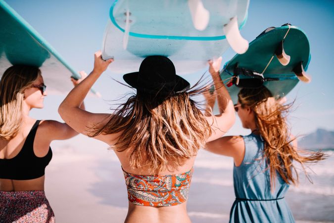 Group of female friends carrying surfboards overhead