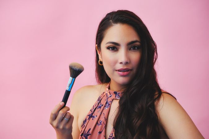 Head shot of elegant Hispanic woman looking at camera while holding large make up brush