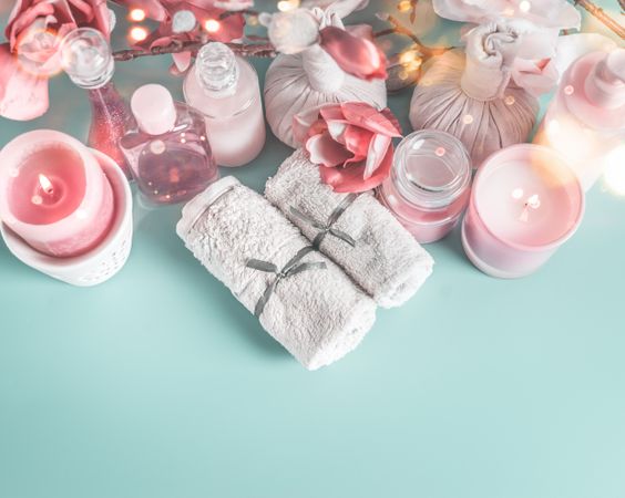 Spa and beauty cosmetic on blue desktop background with towels, candle and pink flowers. Top view