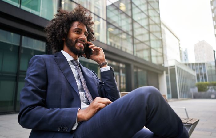 Joyful man in suit sitting outside and talking phone