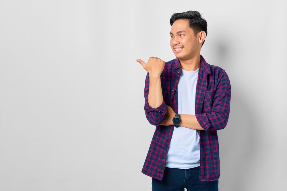 Asian male in grey studio with thumb to the side