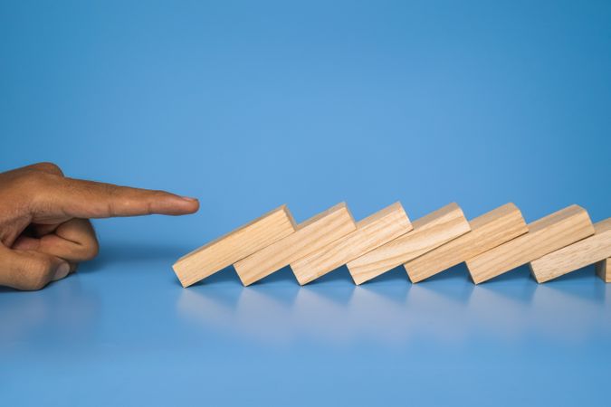male hand drop wooden blocks isolated on blue background. domino effect or risk protection strategy concept