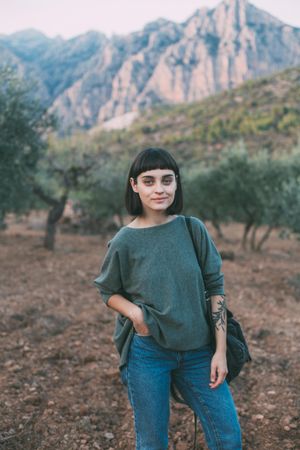 Smiling woman with book bag on shoulders in park with olive trees