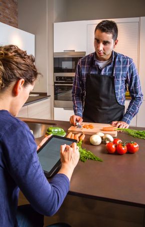 Woman checking digital tablet as her and her partner prepare vegetables for meal