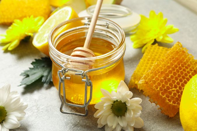 Flowers, lemons, honeycombs, glass jar with honey and dipper on grey background, closeup