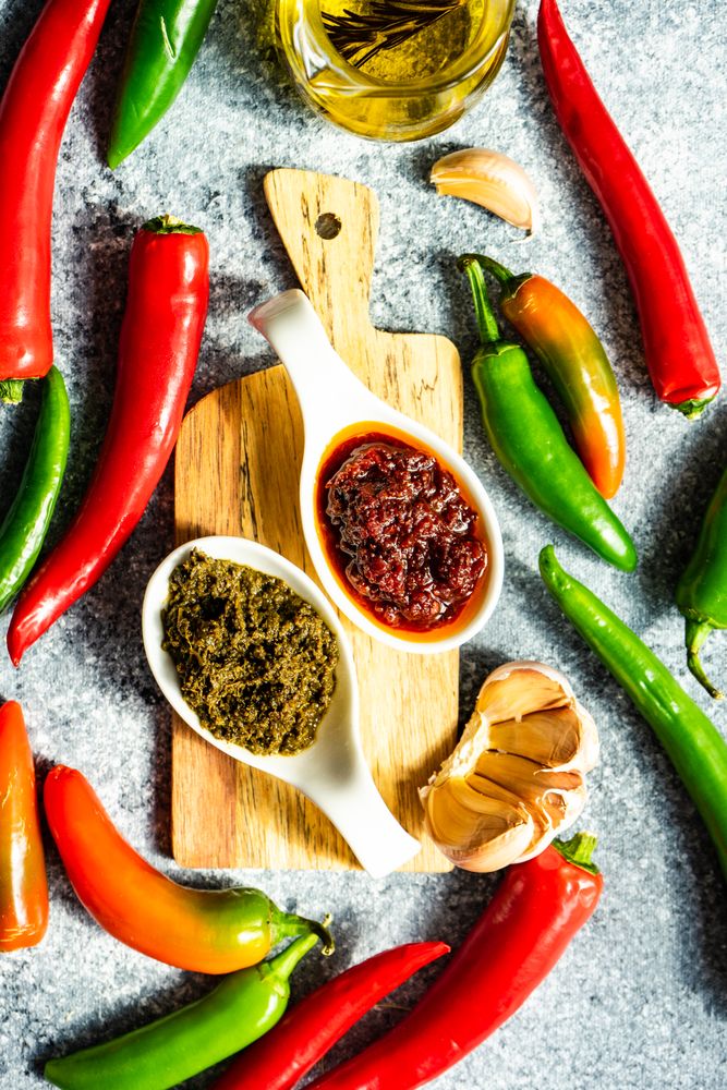 Top view of two servings of Georgian sauce Adjika surrounded by raw ingredients