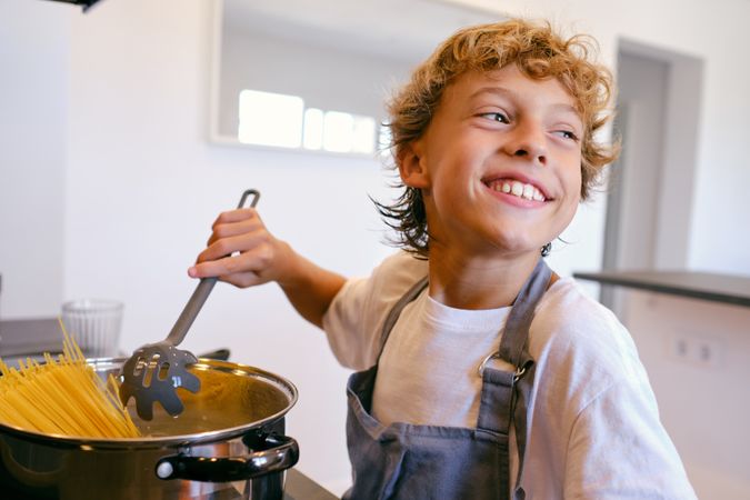 Positive boy cooking spaghetti in pot at home