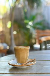 Glass of fresh latte served on saucer with vanilla stick