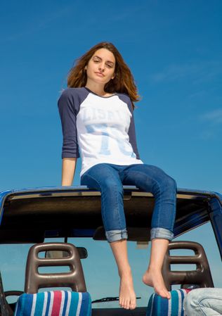Woman barefoot sitting on roof of car