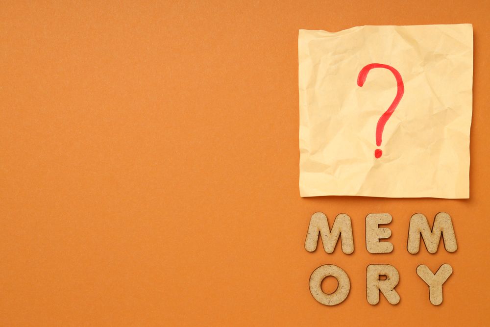 The word “Memory” written in cork below post it note on dusty orange background, copy space