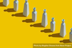 Single row of painted glass bottles on yellow background 0gzr8b