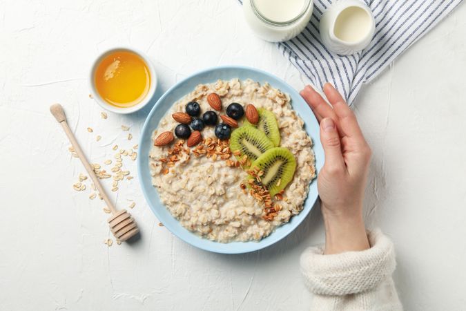 Woman hand holds plate with oatmeal porridge with fruits, top view