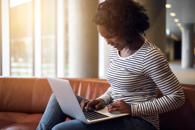 Smiling woman sitting on sofa and smiling at laptop