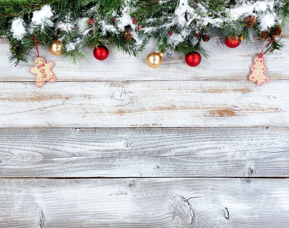 Top border of snowy Christmas evergreen branches with other holiday decorations on rustic wooden boards