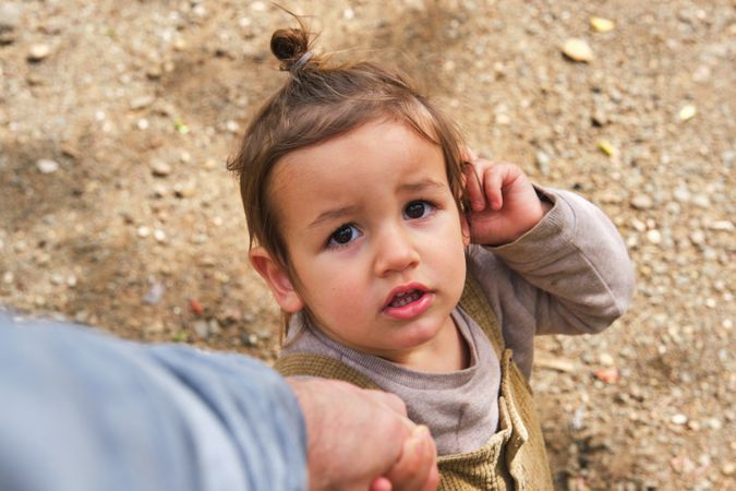 Adorable boy holding parent hand and standing on dirt road