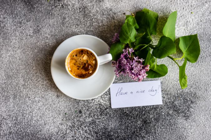 Top view of cup of espresso and lilacs on grey background with a note