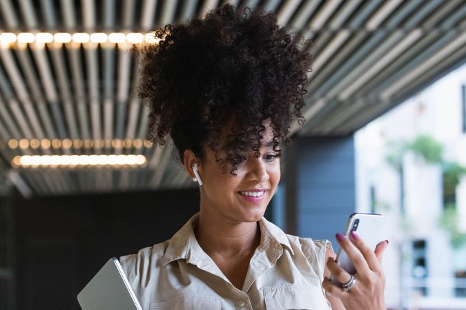 Smiling Black pregnant woman using smartphone and wireless earphones