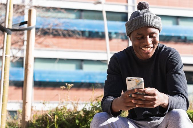 Serious Black man using smartphone sitting on street