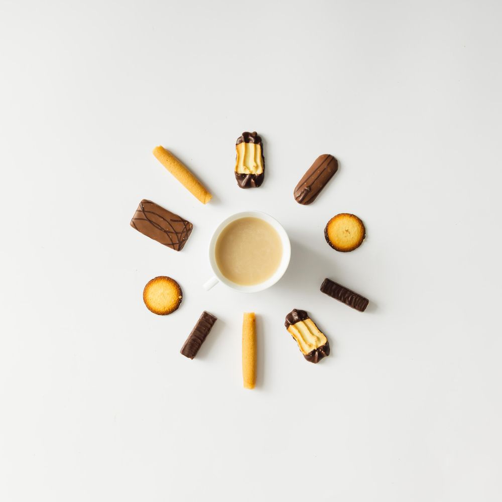 Coffee cup surrounded with cookies on light background