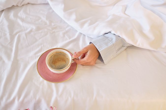 Anonymous female in bed with cup of morning coffee