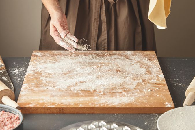 Woman at breadboard with flour between rolling dough
