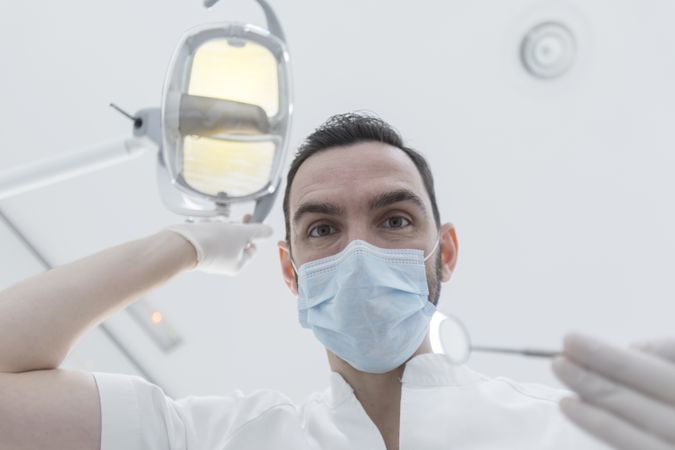 Dentist wearing surgical mask while holding angled mirror, ready to begin exam