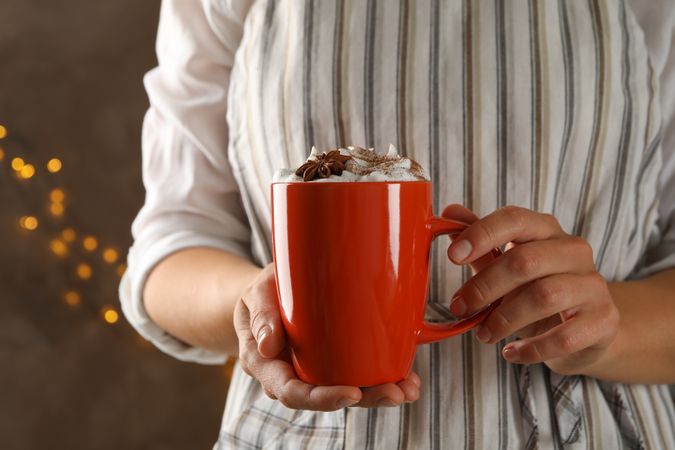 Woman hold cup of pumpkin latte against brown background with blurred lights