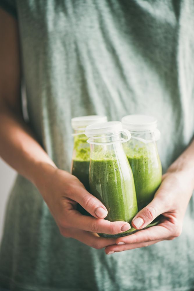 Woman in green dress holding three bottles of green smoothie