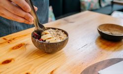 Chef preparing vegetarian breakfast putting banana slices on coconut bowl using metal tongs.