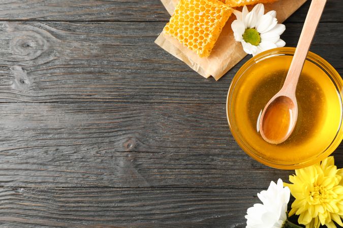Bowl with honey, honeycombs and flowers on wooden background, copy space
