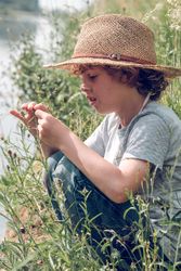 Dreamy boy in straw hat on river shore