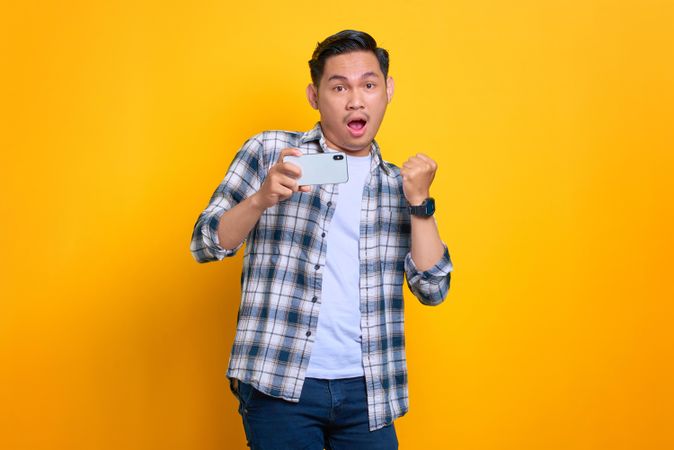 Open mouthed Asian male holding his phone and taking a photo with it