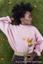 Black woman in pink sweater laying on green grass holding flower 5nKgl4