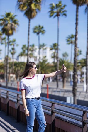 Smiling young woman in sunglasses taking selfie with phone camera on sunny day
