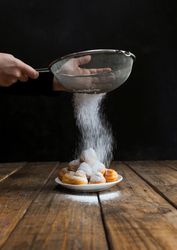 Person sprinkling icing sugar over on cookies