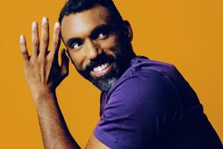 Confident Black man in yellow studio smiling with hand on to his face