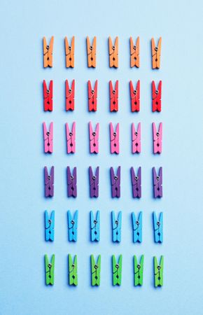 Rainbow colored clothes pins on light blue background