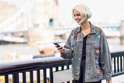 Smiling blonde female listening to podcast on phone along river walk