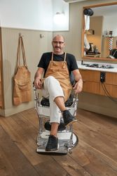 Confident smiling barber sitting on chair in barbershop