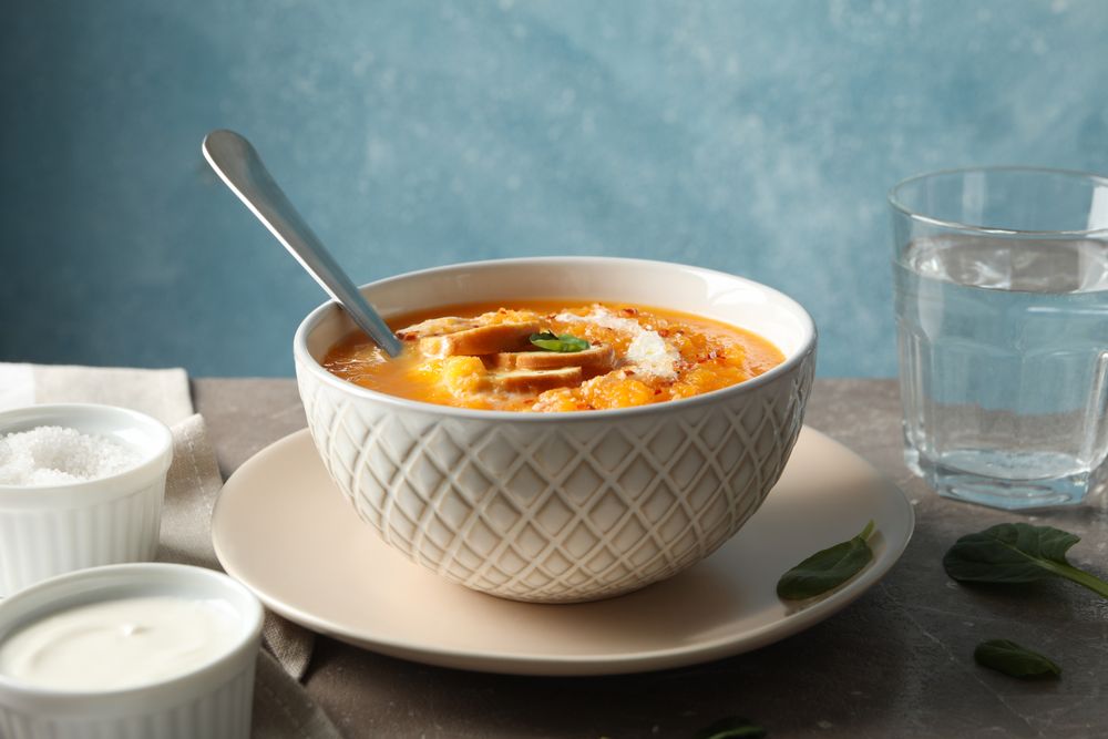 Bowl of delicious pumpkin soup on table with glass of water