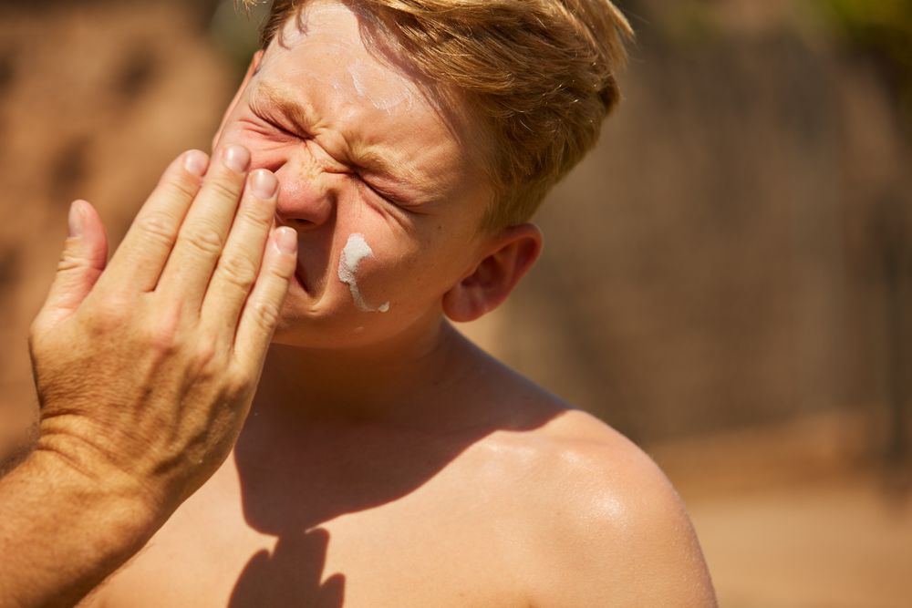 Faceless man applying sun cream on kid
