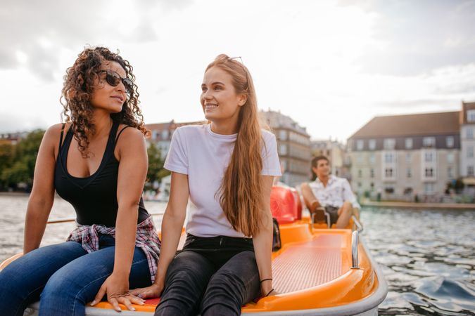 Two young women sitting on pedal boat with a man in background