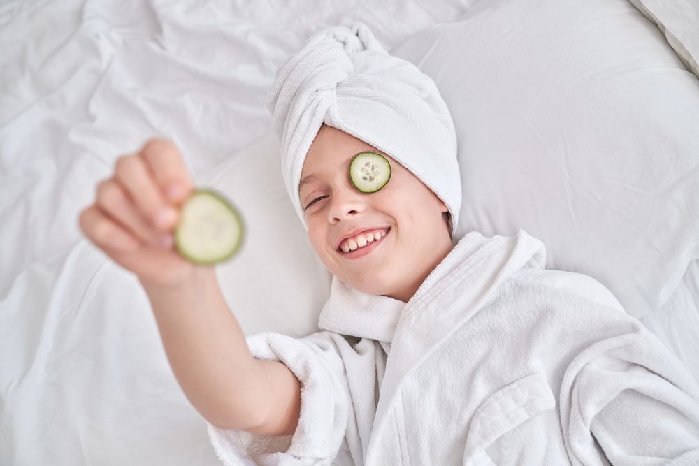 Boy with cucumber slice on eye in bedroom