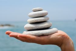 Side view of hand with small pile of rocks with coast in background
