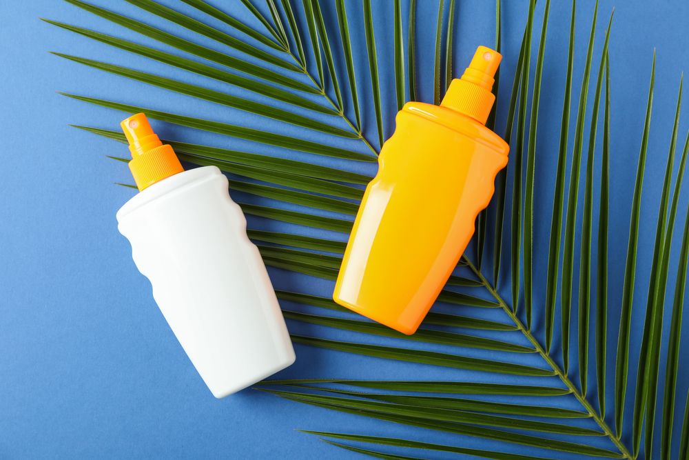 Composition with sunscreen sprays and palm leaf on color background. Top view, closeup