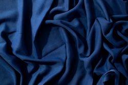 Navy or dark blue fabric wavy spiral crumpled background texture with copy space in the center.